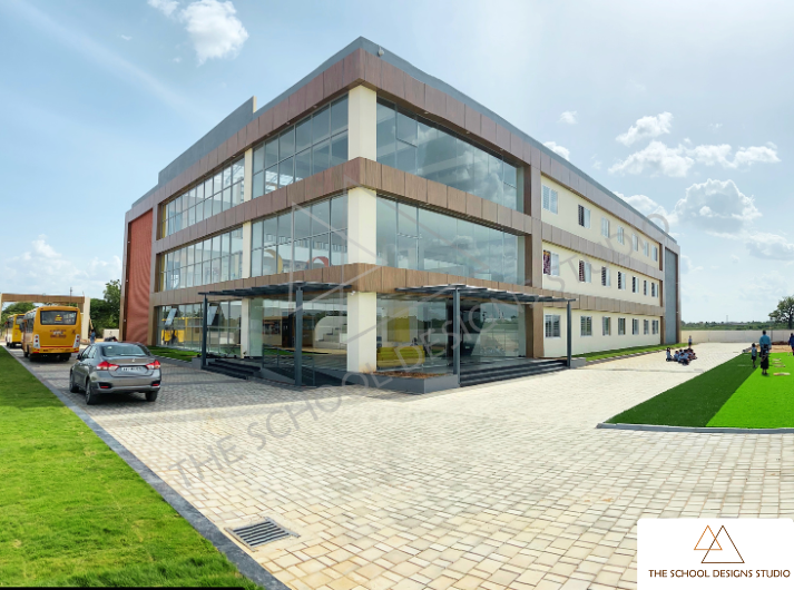 Front elevation of Pragati Vidyalaya, Challakere—a modern school campus designed by The School Designs Studio featuring a contemporary glass façade and landscaped outdoor area.